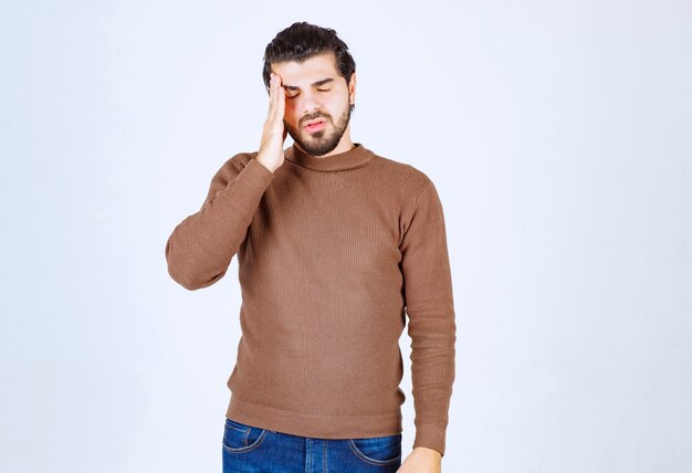 Portrait of a young man thinking and standing against white wall.