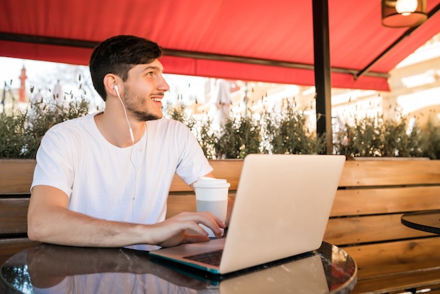 Portrait of young man using his laptop while sitting in a coffee shop. Technology and lifestyle concept.