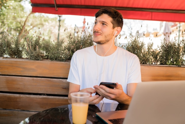 Portrait of young man using mobile phone while sitting in a coffee shop outdoors. Communication concept.