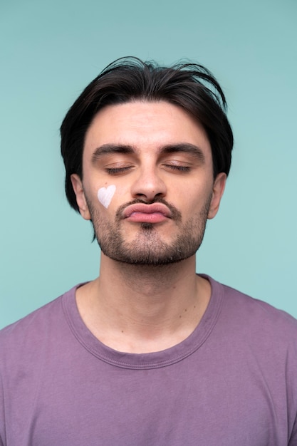 Free photo portrait of a young man wearing a heart on his face made of moisturizer