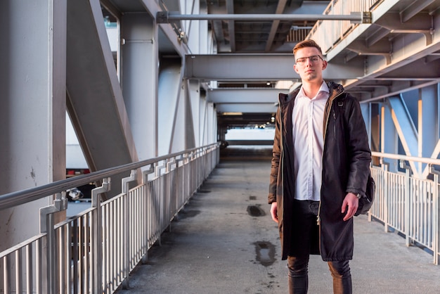 Free photo portrait of a young man wearing long jacket standing on the bridge