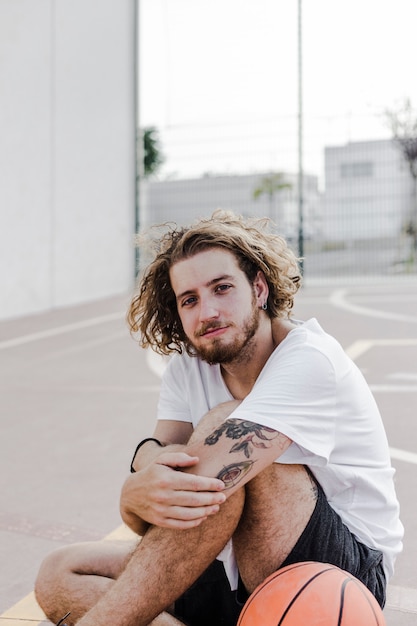 Free Photo portrait of a young man with basketball sitting in court