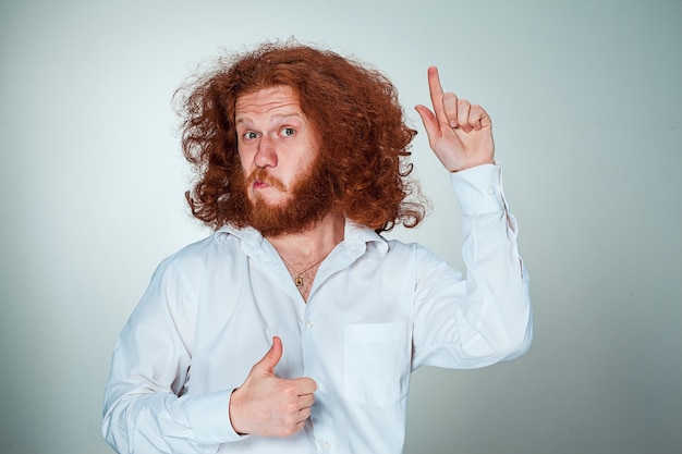 Free photo portrait of young man with long red hair and with shocked facial expression on gray background showing up