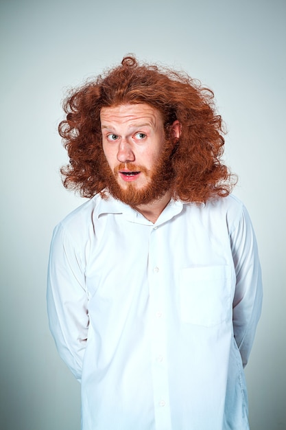 Free photo portrait of young man with long red hair and with shocked facial expression on gray background