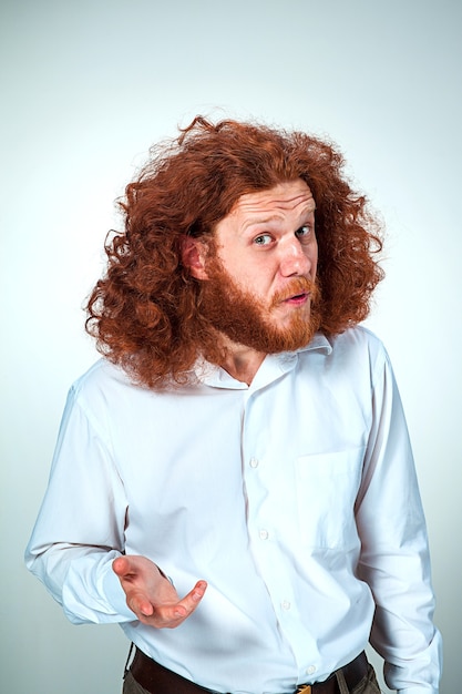 Portrait of young man with long red hair and with shocked facial expression on gray background