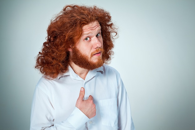 Free Photo portrait of young man with long red hair and with shocked facial expression on gray pointing to itself