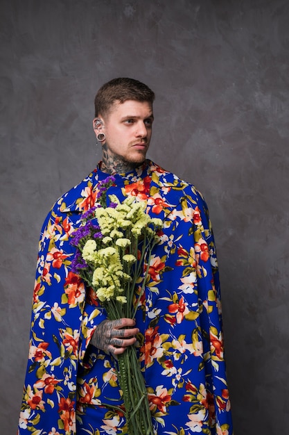 Free photo portrait of young man with pierced ears and nose holding purple and yellow limonium flowers in hand