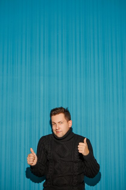 Portrait of young man with serious facial expression showing OK over blue studio background