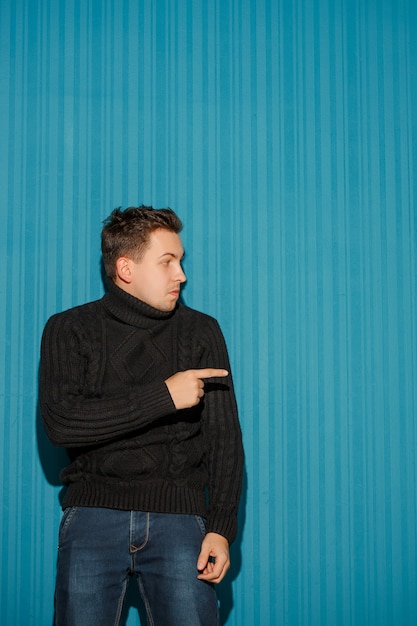 Portrait of young man with serious facial expression showing to the right over blue background