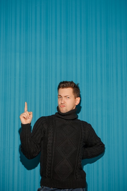 Portrait of young man with serious facial expression showing up over blue studio background