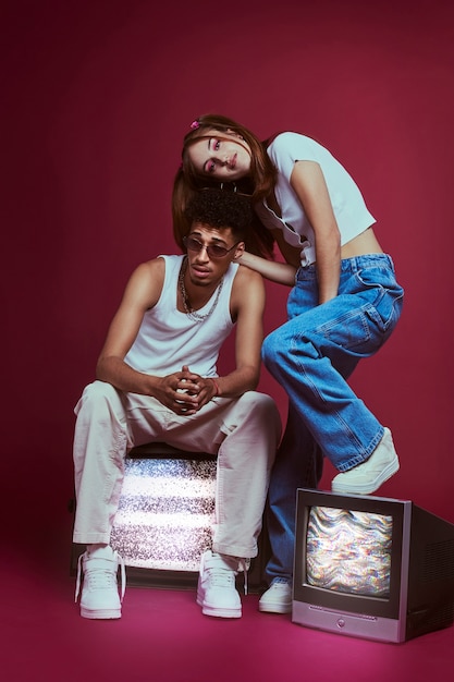 Free photo portrait of young man and woman in 2000s fashion style posing with tv