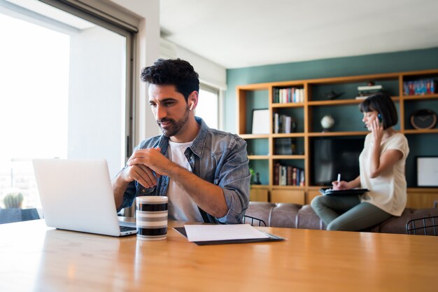 Portrait of young man working with a laptop from home while woman talking on phone