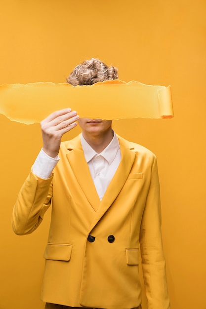 Free Photo portrait of young man  in a yellow scene with torn paper in front of face