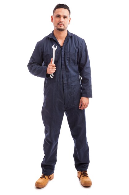 Portrait of a young mechanic wearing overalls and holding a wrench at work on a white background