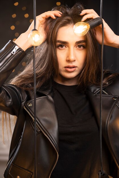 Portrait of a young model in black leather jacket posing near lamps.