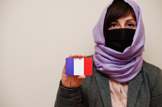 Free photo portrait of young muslim woman wearing formal wear protect face mask and hijab head scarf hold france flag card against isolated background coronavirus country concept