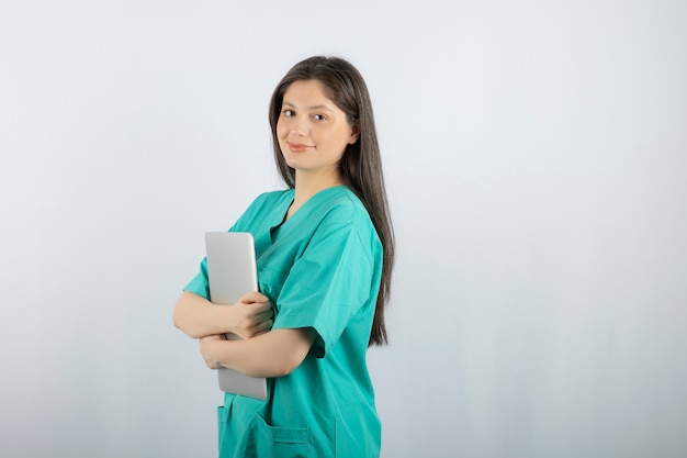 Portrait of young nurse holding laptop on white. 