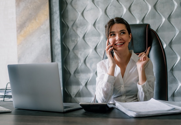 Free Photo portrait of young office worker woman sitting at office desk talking on mobile phone smiling with happy face working process in office