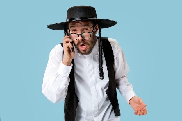 Portrait of a young orthodox jewish man with mobile phone at studio. Purim, business, businessman, festival, holiday, celebration, judaism, religion concept.