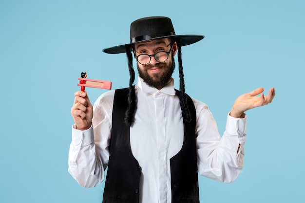 Free photo portrait of a young orthodox jewish man with wooden grager ratchet during festival purim. holiday, celebration, judaism, tradition, religion concept.