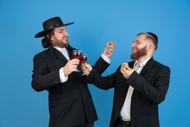 Free photo portrait of a young orthodox jewish men isolated on blue studio wall meeting the passover eating amans ears with wine