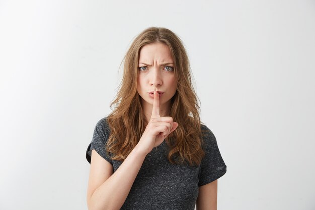 Portrait of young pretty girl frowning straight showing keep silence .