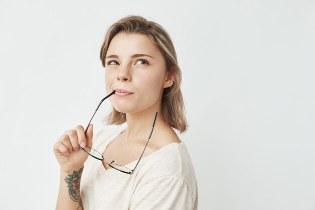 Portrait of young pretty girl smiling thinking dreaming biting glasses .