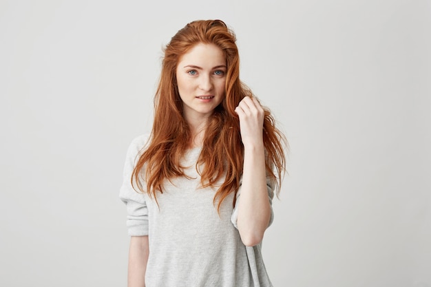 Free photo portrait of young pretty redhead girl with freckles smiling touching hair .