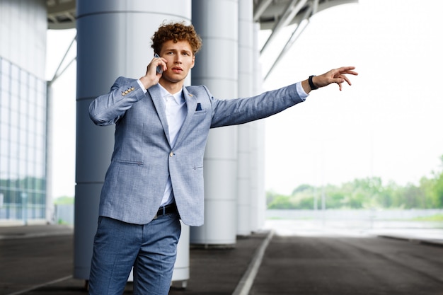 Portrait of young redhaired businessman catching the car and talking on phone