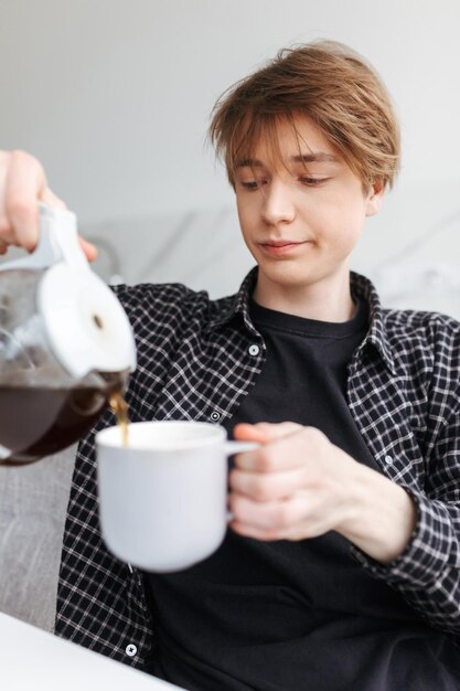 Portrait of young sleepy man sitting and pouring coffee in kitchen at home