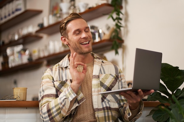 Free Photo portrait of young smiling man coworker joins online meeting from cafe video chats on laptop shows