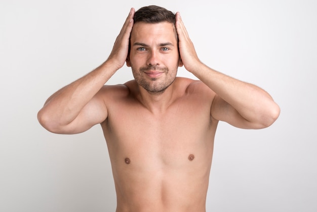 Portrait of young smiling man touching his hair looking at camera standing against white background