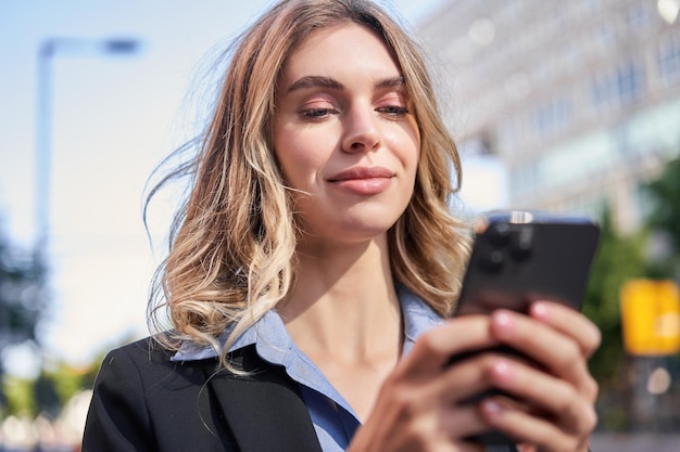 Free photo portrait of young smiling saleswoman businesswoman looking at her mobile phone with pleased face rea