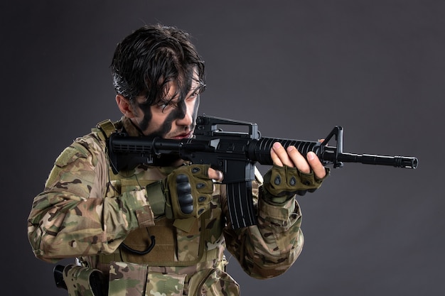 Free photo portrait of young soldier in camouflage aiming machine gun on dark wall