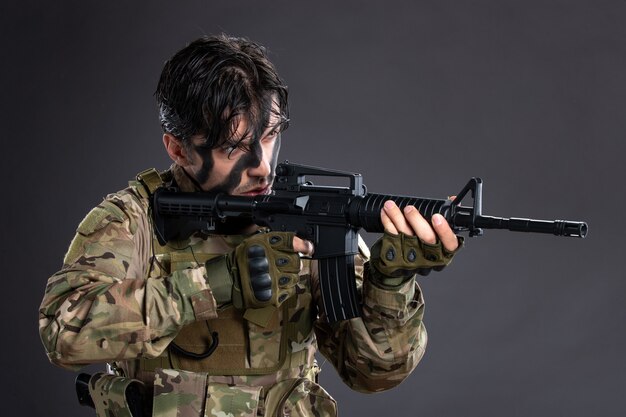 Free Photo portrait of young soldier in camouflage aiming machine gun on dark wall