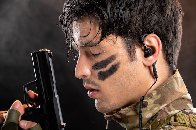 Free photo portrait of young soldier in camouflage holding gun on the black wall