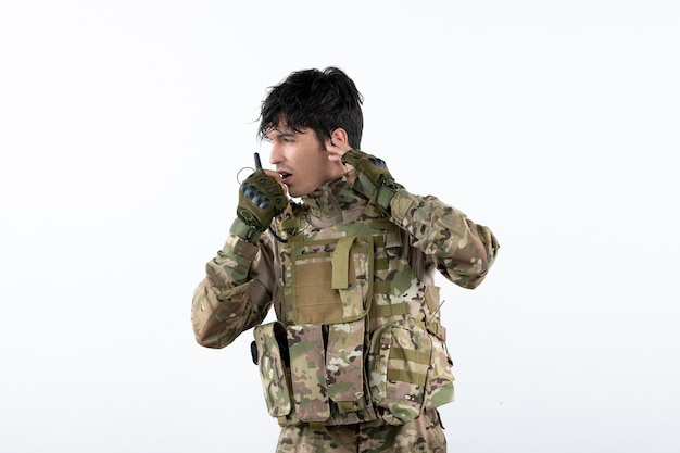 Free photo portrait of young soldier in camouflage talking through walkie-talkie white wall