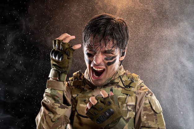 Free photo portrait of young soldier screaming in uniform on the dark wall