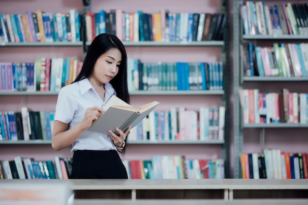 Portrait of young student reading a book in a library