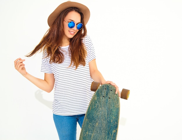 Free photo portrait of young stylish woman model in casual summer clothes in brown hat posing with longboard desk. isolated on white