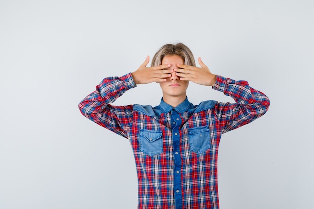 Free Photo portrait of young teen boy covering eyes with hands in checked shirt and looking scared front view