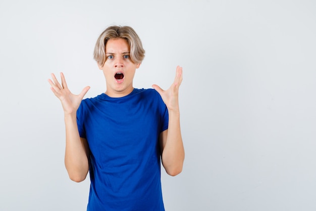 Portrait of young teen boy raising hands while screaming in blue t-shirt and looking terrified front view