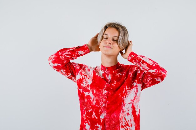 Portrait of young teen boy with hands behind ears, shutting eyes in shirt and looking delighted front view