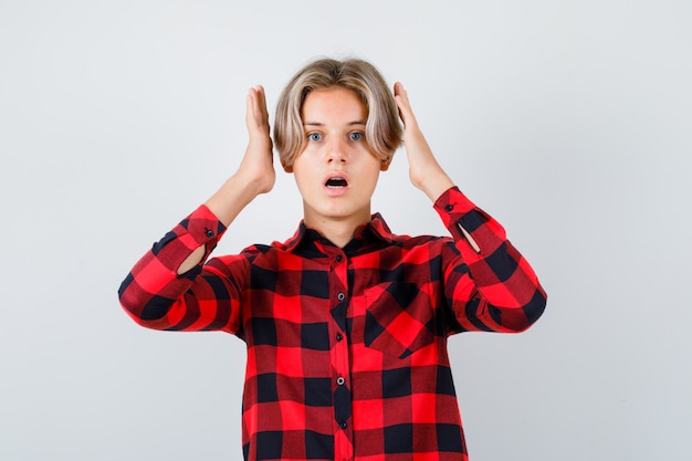 Portrait of young teen boy with hands near head in checked shirt and looking shocked front view