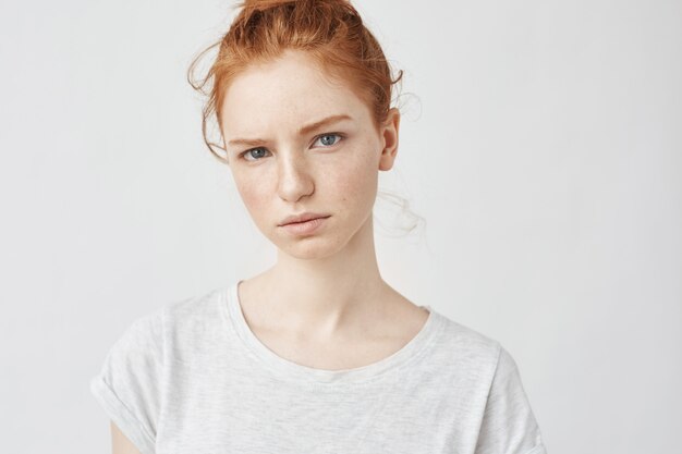 Portrait of young tender redhead woman with healthy freckled skin wearing grey top with serious expression.