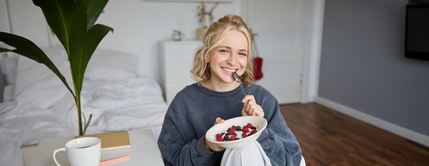 Portrait of young vlogger content creator showing her homemade breakfast on camera eating dessert