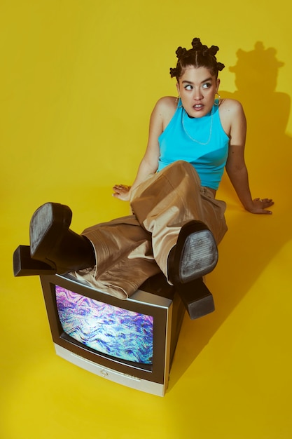 Free photo portrait of young woman in 2000s fashion style posing together with tv