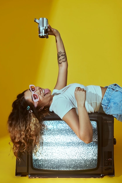 Free Photo portrait of young woman in 2000s fashion style posing with camera and tv