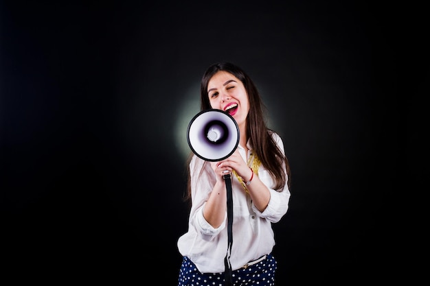 Portrait of a young woman in blue trousers and white blouse posing with megaphone in the studio