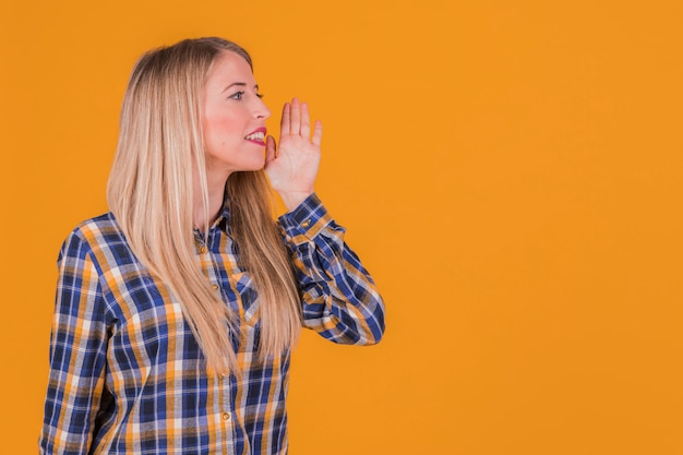 Free photo portrait of a young woman calling someone against an orange backdrop